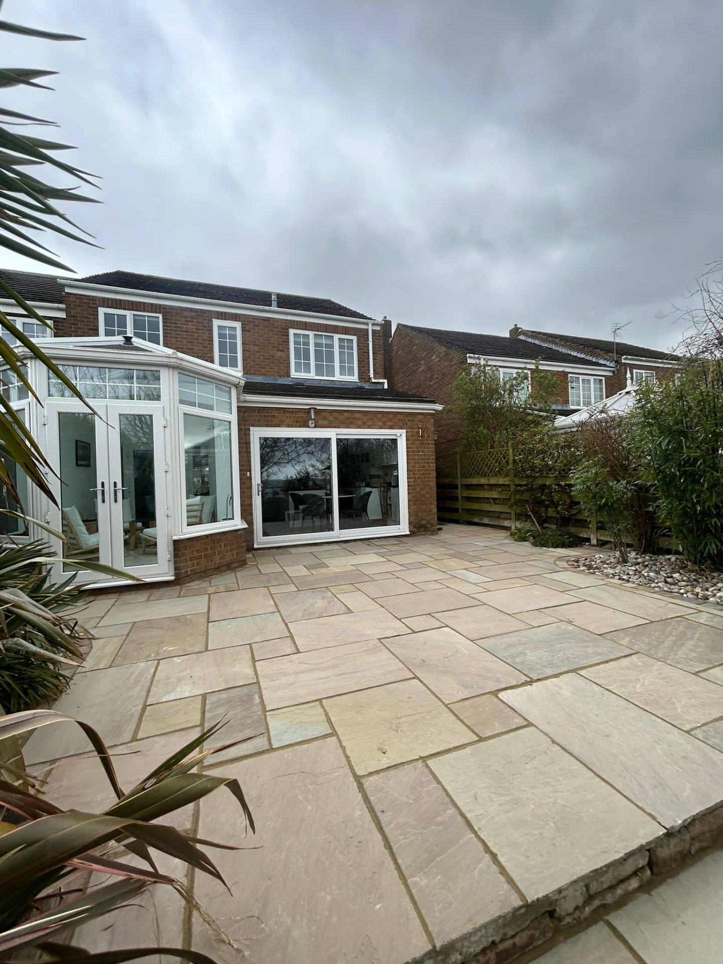 Wide buff Indian sandstone terrace running across the back of a house with a cobble bed edge — The Vale Company